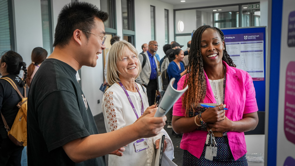 Group of people conversing in a professional setting near a display board with charts.